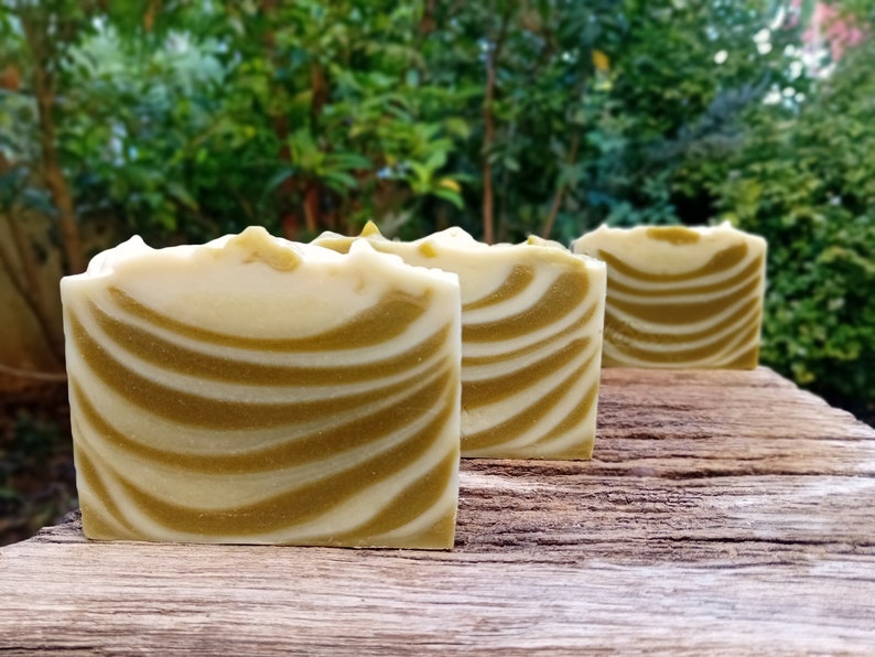 Puede incluir: Tres barras de jab&oacute;n artesanal con un patr&oacute;n de remolino blanco y verde. El jab&oacute;n est&aacute; dispuesto en una fila sobre una superficie de madera.