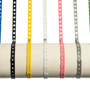 May include: A set of eight metal pipe straps in various colors, including red, blue, black, yellow, white, pink, gray, and green. The straps are all the same size and have a series of holes along their length.