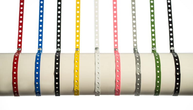 May include: A set of eight metal pipe straps in various colors, including red, blue, black, yellow, white, pink, gray, and green. The straps are all the same size and have a series of holes along their length.