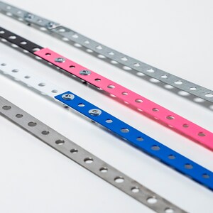 May include: Four metal strips with holes, each painted a different color: silver, black, pink, and blue. The strips are arranged in a diagonal line, with the silver strip at the bottom and the blue strip at the top.