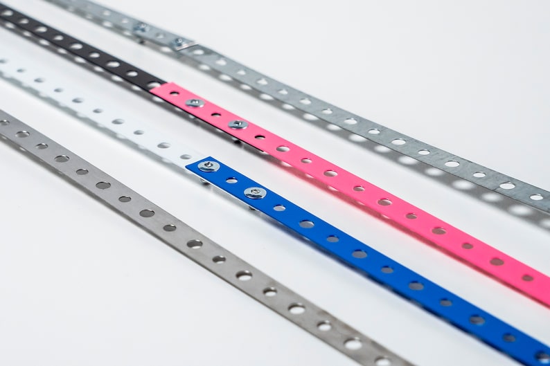 May include: Four metal strips with holes, each painted a different color: silver, black, pink, and blue. The strips are arranged in a diagonal line, with the silver strip at the bottom and the blue strip at the top.
