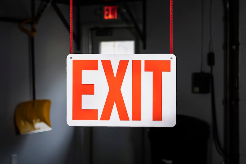 May include: A white sign with red lettering that says "EXIT" hanging from the ceiling.