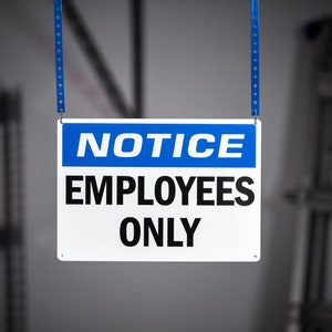 May include: A white sign with blue lettering that reads "NOTICE EMPLOYEES ONLY" hanging from two blue straps.