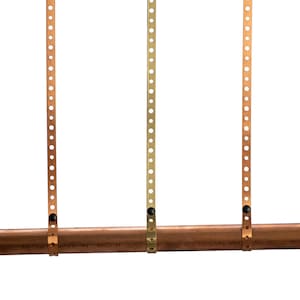May include: Three copper straps with holes are attached to a copper pipe. The straps are secured with black screws.