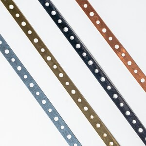 May include: Four metal strips with evenly spaced holes, arranged diagonally. The strips are silver, gold, black, and copper.