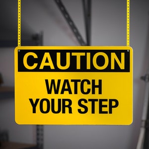 May include: A yellow and black caution sign with the text "CAUTION WATCH YOUR STEP" hanging from a chain.