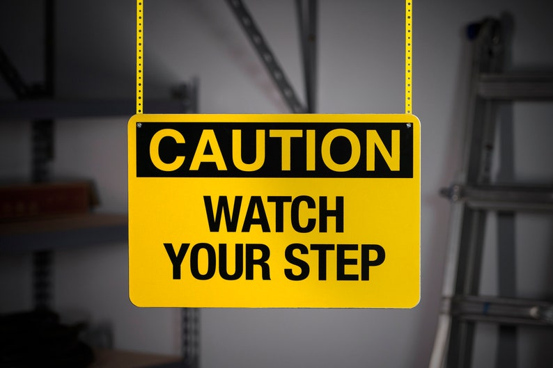 May include: A yellow and black caution sign with the text "CAUTION WATCH YOUR STEP" hanging from a chain.