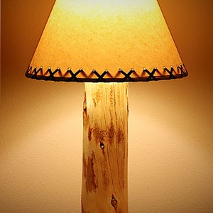 May include: A rustic wooden table lamp with a natural wood base and a brown fabric lampshade with black stitching.