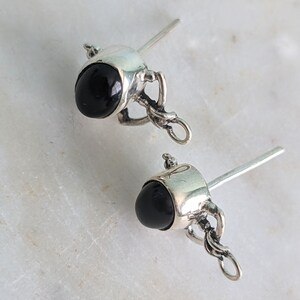 May include: A pair of silver earring findings with black gemstone accents. Each finding has a small loop for attaching a charm or pendant.