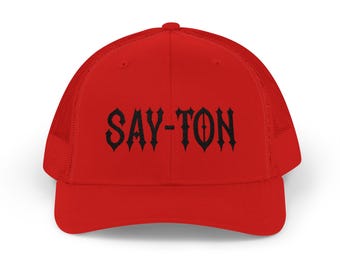 Puede incluir: Gorra de camionero roja brillante con parte trasera de malla y visera curva. La parte delantera presenta el texto negro "SAY-TON" en una fuente gótica. Esta gorra es de estilo clásico, adecuada para uso casual.