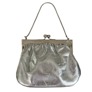 May include: Silver clutch bag with a metal frame and handle. The bag has a textured, crinkled appearance. The handle is a thin, silver metal. The clasp is a silver metal ball closure.