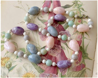 May include: A pastel-colored beaded necklace with a mix of light blue, purple, pink, and green beads. The necklace is made of smooth, oval-shaped beads and is strung on a silver chain.