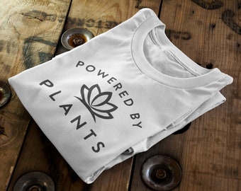 Puede incluir: Camiseta blanca con un gráfico de flor de loto negro y el texto "Powered by Plants".