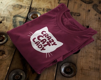 Könnte beinhalten: Ein maroonfarbenes T-Shirt mit einer weißen Katzen-Silhouette und dem Text "Crazy Cat Lady" auf der Vorderseite.