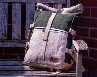 May include: A green and beige canvas backpack with a roll-top closure and adjustable straps. The backpack has a zippered pocket on the front and a large main compartment.