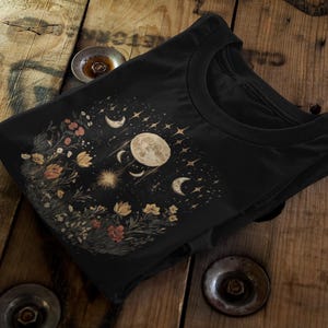 Puede incluir: Camiseta negra con un diseño floral y una impresión de luna creciente y estrellas.