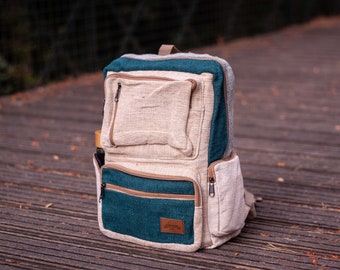 Könnte beinhalten: Ein beige- und blaugrüner Hanfrucksack mit mehreren Taschen und Reißverschlüssen. Der Rucksack steht auf einer Holzoberfläche.