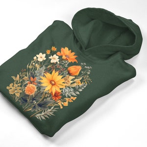 Peut inclure: Un sweat à capuche vert foncé avec un imprimé floral composé de fleurs orange, jaunes et blanches. Les fleurs sont disposées en forme de bouquet.