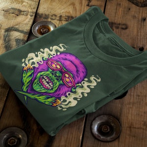 May include: Green and purple cartoon gorilla wearing sunglasses and smoking a joint. The gorilla is surrounded by green smoke and is on a dark green t-shirt.