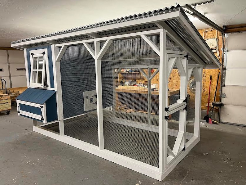 May include: A white and blue chicken coop with a metal roof and a wire mesh enclosure. The coop has a nesting box and a door with a latch.