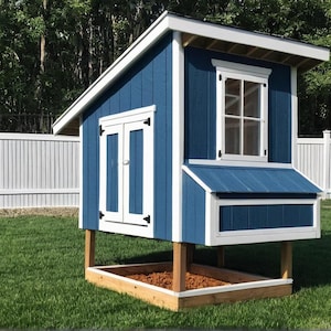 May include: A blue and white wooden chicken coop with a pitched roof, window, and double doors. The coop is elevated on wooden posts and sits on a grassy lawn, with a white fence and trees in the background.