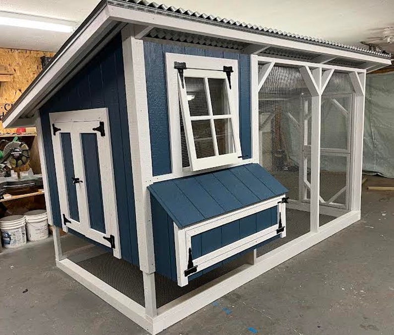 Blue chicken coop with white trim, an enclosed run for chickens and 2 windows.