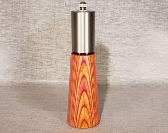 May include: A wooden pepper mill with a stainless steel top. The base is a vibrant blend of red, orange, and yellow wood grain. The mill has a conical shape, widening from the top to the base. A small, silver knob sits atop the stainless steel cylinder.