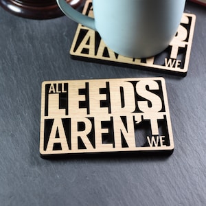 May include: Two wooden coasters with black lettering. The top coaster says "All Leeds Aren't We" and the bottom coaster says "All Leeds Aren't We".