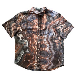 May include: A short-sleeve button-down shirt featuring a marbled tie-dye pattern in shades of dark brown, charcoal gray, and white. The garment has a standard collar, a front button placket with light-colored buttons, and a single chest pocket.