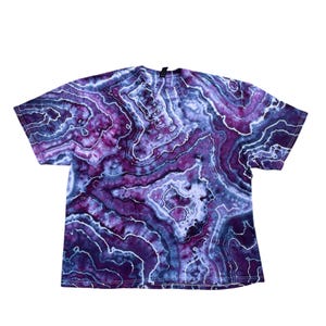 May include: A short-sleeved t-shirt with a tie-dye pattern in shades of purple, blue, and white. The design features a marbled effect with swirling lines and color variations. The shirt is made of a soft material and has a crew neck.