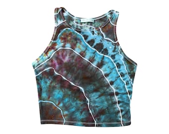 Pode incluir: Um top de tanque tie-dye com um esquema de cores azul, verde, marrom e roxo. O top tem um estilo racerback e um comprimento cropped.