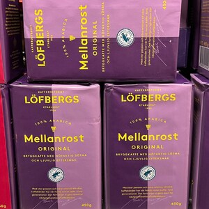 Könnte beinhalten: Mehrere Packungen LÖFBERGS Mellanrost Original Kaffee, in Lila- und Lavendeltönen. Die Verpackung enthält gelben Text mit der Aufschrift "100% Arabica" und "450g". Die Packungen zeigen auch ein Logo und Text auf Schwedisch.