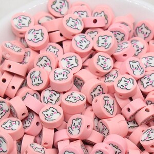 May include: A bowl filled with pink and white round beads with a cartoon animal face on each bead.