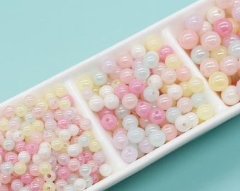 May include: A white ceramic dish with three sections filled with pastel pink, yellow, and white iridescent round beads.
