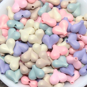 May include: A bowl filled with pastel-colored heart-shaped beads. The beads are in shades of pink, purple, blue, and cream.