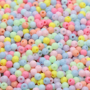 May include: A bowl filled with pastel-colored plastic beads. The beads are in shades of pink, blue, yellow, and green.