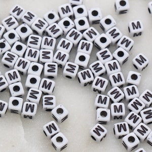 May include: A large pile of white plastic letter beads with the letter "M" printed in black on each bead.