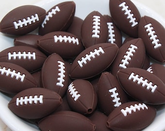 May include: A white bowl filled with brown football-shaped silicone charms. The charms have white stitching details.