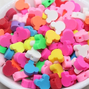 May include: A bowl filled with colorful plastic Mickey Mouse head shaped beads. The beads are in a variety of colors, including red, pink, yellow, green, blue, and purple.