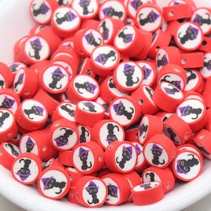May include: A bowl filled with red round beads with a white circle and a black cat wearing a purple hat printed on each bead.