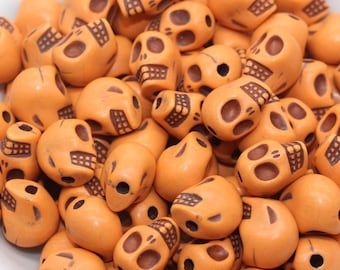 Peut inclure: Un bol rempli de perles orange en forme de crâne. Les perles ont des détails bruns et sont parfaites pour la création.