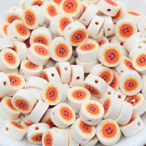 May include: A bowl filled with white ceramic beads with a smiling sun design in orange and yellow.