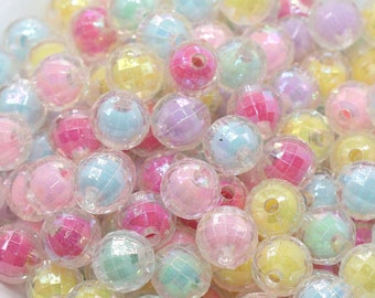 May include: A bowl filled with iridescent pastel-colored plastic beads. The beads are round and have a faceted design.