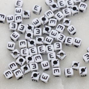 May include: A large quantity of white plastic letter beads, each bead is a cube with the letter "E" printed on each side in black.