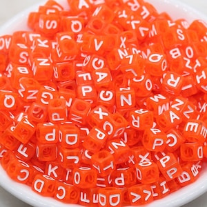 May include: A white bowl filled with orange letter beads. The beads are made of plastic and have white letters on them. The letters are all different and include the letters A, B, C, D, E, F, G, H, I, J, K, L, M, N, O, P, Q, R, S, T, U, V, W, X, Y, and Z.