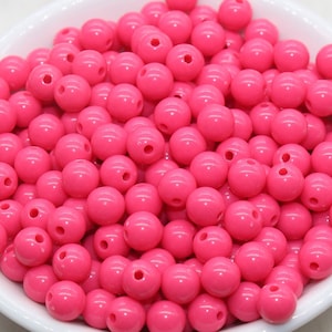 May include: A bowl filled with bright pink round plastic beads. The beads have two holes for stringing.