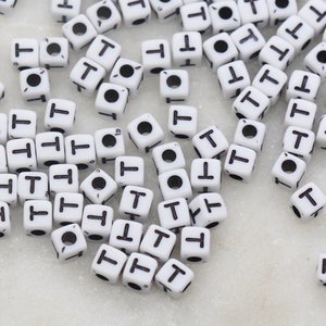 May include: A large quantity of white plastic letter beads with the letter "T" printed in black on each bead.