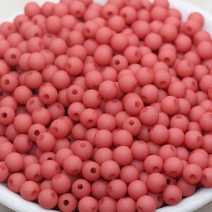 May include: A bowl filled with coral-colored round beads. The beads are smooth and have a matte finish.