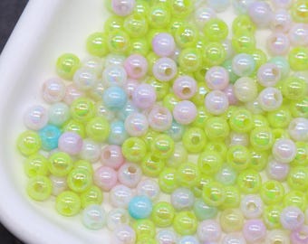May include: A collection of small, iridescent beads in a white tray. The beads are primarily light green, with accents of pink, blue, and white. These beads are likely used for jewelry making or other craft projects.