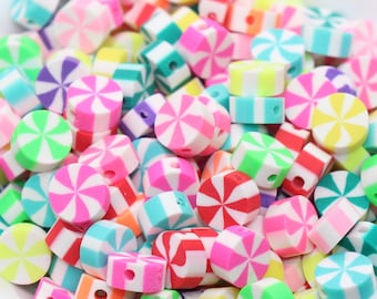 Puede incluir: Un bol lleno de cuentas de colores con forma de bastón de caramelo. Las cuentas están hechas de arcilla polimérica y tienen una base blanca con rayas de color rosa, azul, verde, amarillo y morado.
